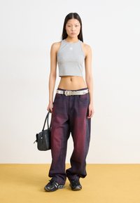 Gray cropped tank top with logo, dark denim pants with ombre red tones, silver belt, black bag, and running shoes with a textured finish.