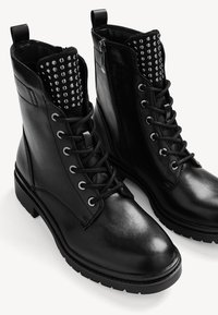 Bottes en cuir noir à la cheville avec lacets, fermeture éclair latérale et détail de languette cloutée, dotées d'une semelle en caoutchouc épaisse pour plus de durabilité.
