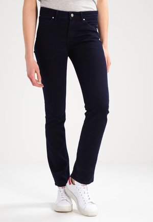 Donkerblauwe, rekbare denim jeans met een slim fit, vijf zakken, riemlussen en zilveren hardware. Gecombineerd met witte sneakers.