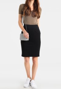Black pencil skirt paired with an olive green short-sleeve top. Model wears white sneakers and holds a small gray handbag.