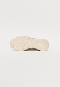 Suela de zapato deportivo de color beige claro con surcos y patrones texturizados para mayor tracción; el talón redondeado y los bordes curvados mejoran el agarre.