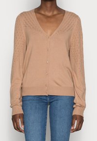 Cárdigan de punto beige con escote en V, con mangas de patrón de diamantes, cierre frontal con botones y puños acanalados. Textura ligera y suave.