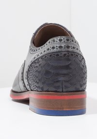 Scarpa nera in pelle con un motivo testurizzato e squamoso sul tallone, cuciture dettagliate e una suola impilata multicolore in rosso e blu.