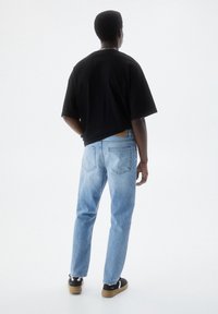 Maglietta nera oversize, jeans in denim azzurro chiaro con effetto sbiadito, e sneakers nere con dettagli bianchi. Vista posteriore.