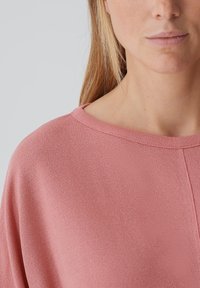 Rosa, texturiertes Oberteil mit rundem Halsausschnitt und lockerer Passform. Der Stoff wirkt leicht und weist subtile Nähte auf.