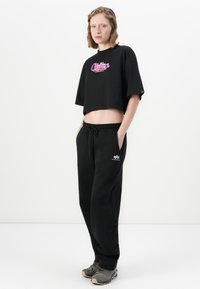 Musta lyhyt t-paita, jossa on värikäs graafinen kuvio, yhdistettynä mustiin collegehousuihin, joissa on kiristysnyöri vyötäröllä ja sivutaskut. Harmaat lenkkarit.