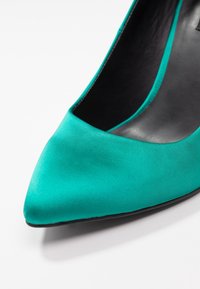 Tyrkysová saténová lodička na vysokém podpatku s špičatou špičkou a hladkým černým interiérem. Hladký povrch s ostrým designem.