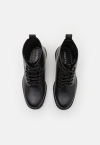 Botas de cuero negras hasta el tobillo con un acabado suave, punta redondeada, diseño con cordones y suelas de goma resistentes. Presentan un logo en las plantillas.