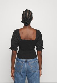 Top nero con arriccio, maniche corte a palloncino e schiena quadrata, abbinato a jeans blu a vita alta con la caratteristica cucitura della tasca posteriore.