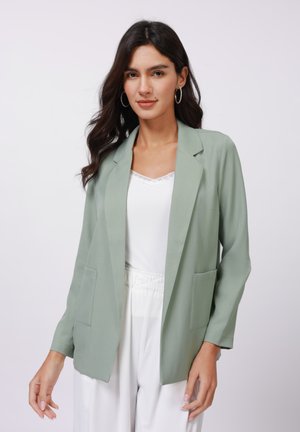 Light green blazer in a smooth fabric, featuring a notched lapel, open front, and two front pockets. Styled over a white top.