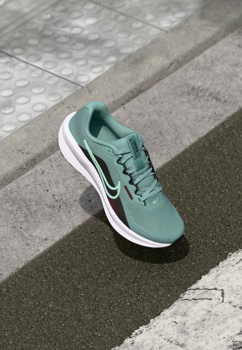 Nike Laufschuhe aus mintgrünem Mesh, mit schwarzen und rotbraunen Akzenten, weißer Sohle, strukturiertem Obermaterial und gepolstertem Innenraum.