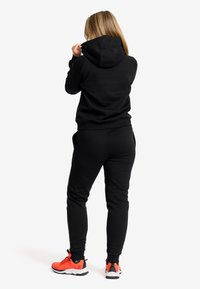 Svart hoodie och joggers gjorda av mjukt tyg, med en avslappnad passform och sidofickor, tillsammans med klara orangea träningsskor.