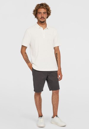 Polo bianco con colletto, abbinato a pantaloni corti grigi scuri. Il modello indossa scarpe da ginnastica bianche. Presenta maniche corte e una sottile texture.