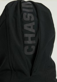Sudadera negra con capucha y cuello con cremallera, con "CHASING" impreso en gris oscuro en el lado izquierdo. Tela suave con una textura agradable.