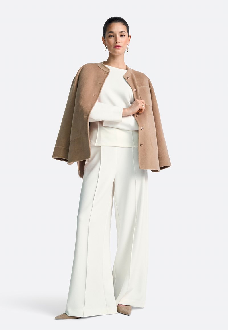 Bēša vilnas apmetnis ar pogām, balta slāņaina blūze un platas baltas bikses ar priekšējām šuvēm. Izskatu papildina nūda krāsas augstpapēžu kurpes.