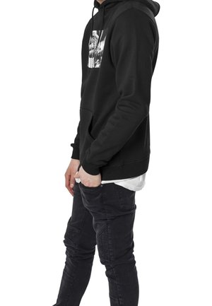 Sudadera negra de tejido suave con bolsillo tipo canguro y un estampado gráfico en el pecho. Combinada con vaqueros oscuros que presentan detalles texturados.