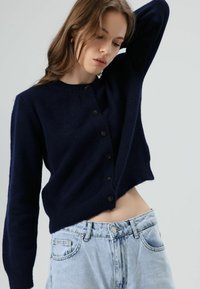 Marineblauw cropped vest met een ronde halslijn, voorzien van zwarte knopen aan de voorkant en een zachte, gestructureerde gebreide stof.