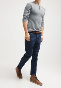 Šedá dlouhá rukávová henley košile s knoflíkovými detaily, námořnické modré chino kalhoty a hnědé šněrovací kotníkové boty s hladkým povrchem a texturovanými tkaničkami.