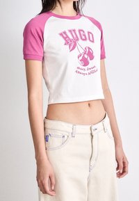 Camiseta blanca corta con mangas en color rosa y un gráfico de cereza acompañado de texto, junto con unos pantalones cortos de mezclilla de cintura alta en un tono claro.