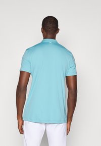 Lyseblå kortermet polo skjorte med krage, laget av glatt stoff. Bak har den en liten logo ved nakkeområdet. Enkel design.