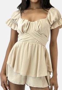 Beige Peplum-Top mit kurzen, gerafften Ärmeln und einem Wickelbund in der Taille. Weicher Stoff mit einem ausgestellten Saum und einem geschichteten Design, das eine glatte Textur zeigt.