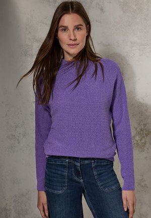 Maglione a coste viola con collo alto e maniche lunghe, abbinato a jeans blu scuro. La texture è morbida e il fit è leggermente rilassato.
