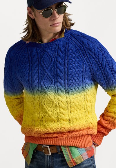 Strikket sweater med blå til gul gradient og kabelstrik design samt orange ribkant. Laget over en ternet skjorte.