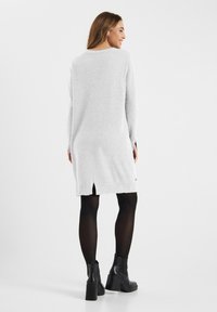 Grijze gebreide jurk met een split aan de achterkant, lange mouwen en een ronde halslijn, gecombineerd met zwarte enkelboots en panty. Glad textuur.