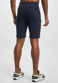 Bermudas de entrenamiento azul marino hechas de tela suave, con cintura elástica y bolsillos laterales. Combinadas con zapatillas deportivas verdes y blancas.