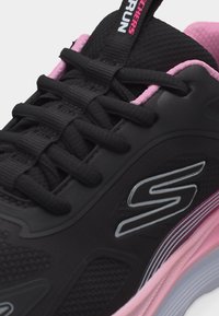 Μαύρο και ροζ αθλητικό παπούτσι Skechers με μαύρα κορδόνια, ανώτερο μέρος από δίχτυ και λογότυπο στο πλάι, λεπτομερή κοντινή εικόνα της γλώσσας και των οφθαλμών.