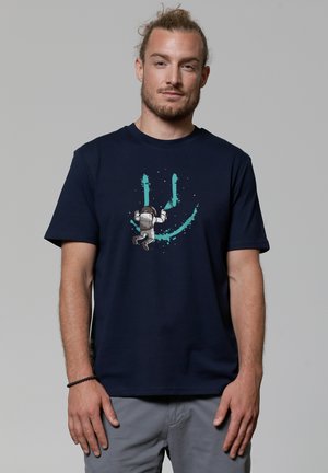 Marineblauw katoenen t-shirt met een grafisch ontwerp van een astronaut tegen een turquoise, spetterstijl ontwerp, ronde halslijn en korte mouwen.