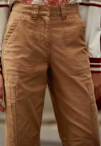 Brune cargo bukser med en tekstureret overflade, høj talje og forlommer med synlige syninger. Enkelt og funktionelt design.