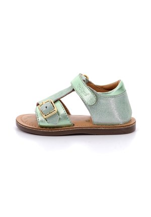 Sandal de cuero verde con un acabado brillante, que presenta una correa de velcro y un detalle de hebilla dorada. Suela plana, diseño abierto en la parte trasera para mayor transpirabilidad.