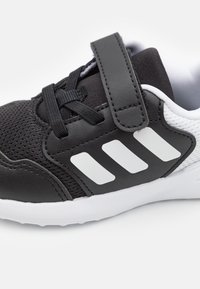 Chaussure de sport noire avec une tige en maille et des accents en synthétique, dotée d'une sangle Velcro et d'un détail logo trois bandes blanches sur le côté.