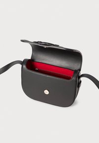 Borsa a tracolla in pelle nera con forma arrotondata, interno rosso, tasca con zip e chiusura a bottone dorato. Dotata di una lunga tracolla regolabile.