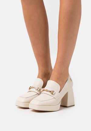 Mocassins en cuir beige avec une finition texturée, bouts carrés et talons blocs. Présente des accents décoratifs en métal doré.