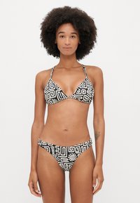 Schwarz-weißes Bikini mit geometrischem Muster. Dreieckiger Oberteil mit dünnen Trägern, passende hüfthohe Unterteile mit ähnlichem Design.