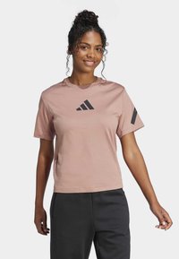 Camiseta de manga corta de color rosa claro, con cuello redondo, que presenta un logo negro en la parte delantera y detalles en negro en las mangas. Material de algodón suave.