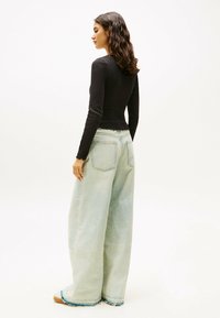 Top nero a maniche lunghe abbinato a jeans a gamba larga blu chiaro con orlo sfrangiato e tasche posteriori. Tessuto morbido con una silhouette aderente.