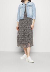 Veste en denim bleu clair sur une robe noire à fleurs, associée à des baskets blanches. Tissu texturé et design mi-long.