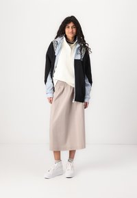 Svart og lyseblå vindjakke med striper, kremfarget skjorte, beige skjørt og hvite høyhælte sneakers. Stoffet virker glatt og lett.