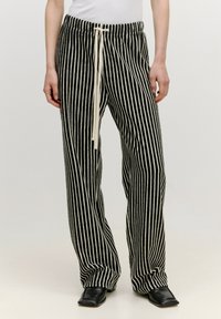 Pantalon à rayures noires et blanches avec taille à cordon, coupe large et texture douce, associé à des chaussures plates noires.