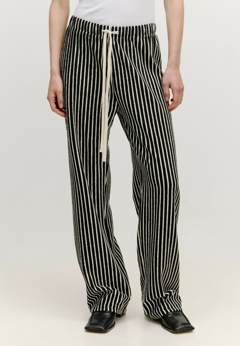 Pantalon à rayures noires et blanches avec taille à cordon, coupe large et texture douce, associé à des chaussures plates noires.