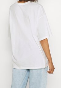 Bílý oversized bavlněný tričko s krátkým rukávem, kulatým výstřihem a volným střihem. Hladká textura bez viditelných vzorů nebo akcentů.