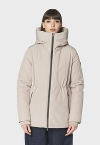 Chaqueta acolchada color beige claro con un cuello alto, cintura ceñida y cierre de cremallera. Presenta bolsillos laterales y puños de manga elásticos. Textura suave.