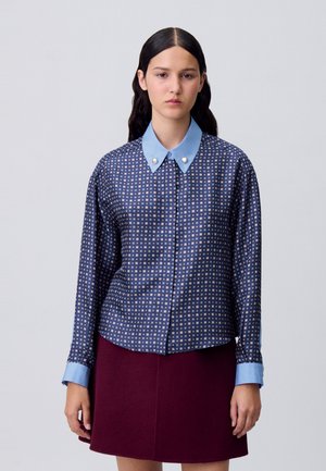 Chemise bleu marine avec un col géométrique bleu clair, présentant un motif en grille avec de petits carrés et deux boutons nacrés sur le col.
