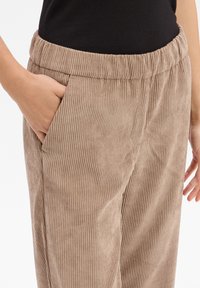 Beige corduroy broek met een ribbelstructuur, voorzien van een elastische tailleband en zijzakken, weergegeven op taillehoogte.
