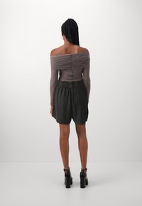 Grijze off-shoulder top met gerimpelde details, gecombineerd met zwarte shorts met een elastische tailleband en een ontspannen pasvorm, afgerond met hakken.