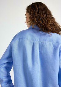 Camicia azzurro chiaro a maniche lunghe realizzata in tessuto morbido con una vestibilità comoda. Presenta un yoke posteriore e una trama sottile sulla superficie.