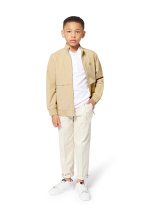 Giacca beige con zip e tasche, polo bianca, pantaloni crema a gamba stretta e sneakers bianche con dettagli neri. Design semplice e vestibilità casual.